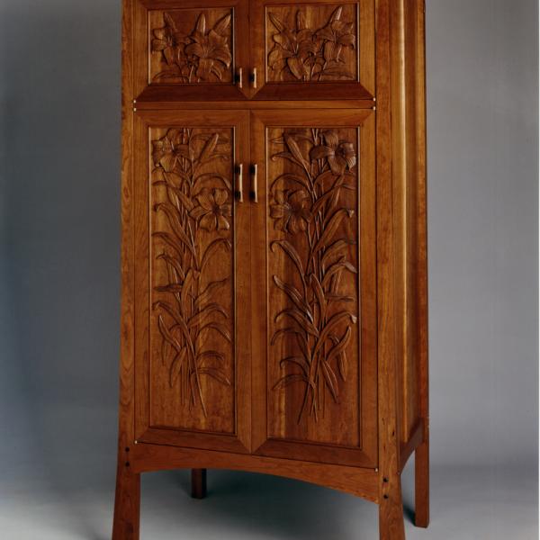 Lily Cabinet. Solid cherry Arts and Crafts style cabinet with hand carved lilies accented by custom made pulls and contrasting wenge tenon pegs.